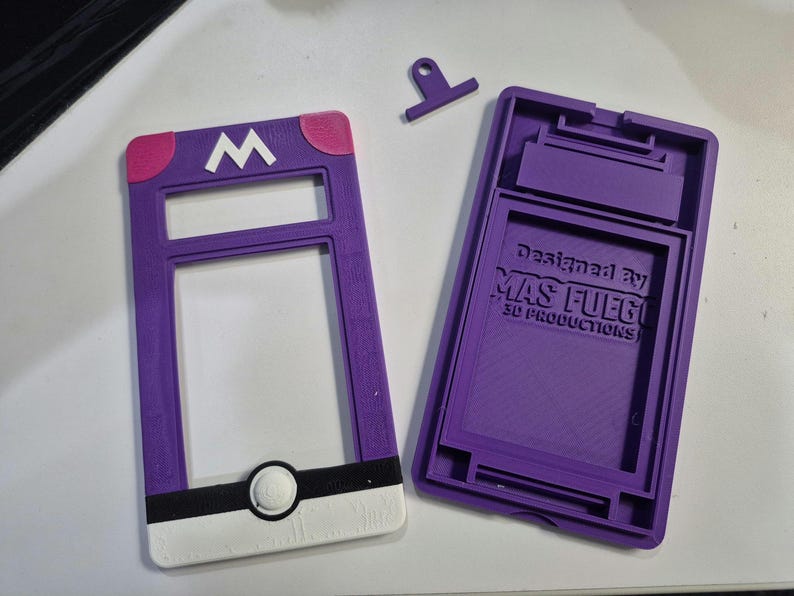 May include: A purple and white 3D-printed case, featuring a white "M" logo and a circular design. The case is designed to hold a device and has the text "Designed By MAS FUEGO 3D PRODUCTIONS".