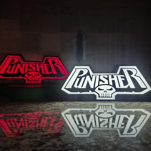 May include: Two illuminated "Punisher" logos. One glows red, the other white. Each features the word "Punisher" above a skull emblem. The logos are on a dark surface, with reflections visible.