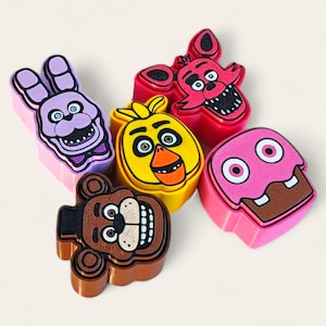 May include: A collection of colorful character-shaped figurines. The figurines include a purple bunny, a red fox, a yellow chick, a brown bear, and a pink cupcake. Each figurine has a unique design and facial expression, with black and white details.