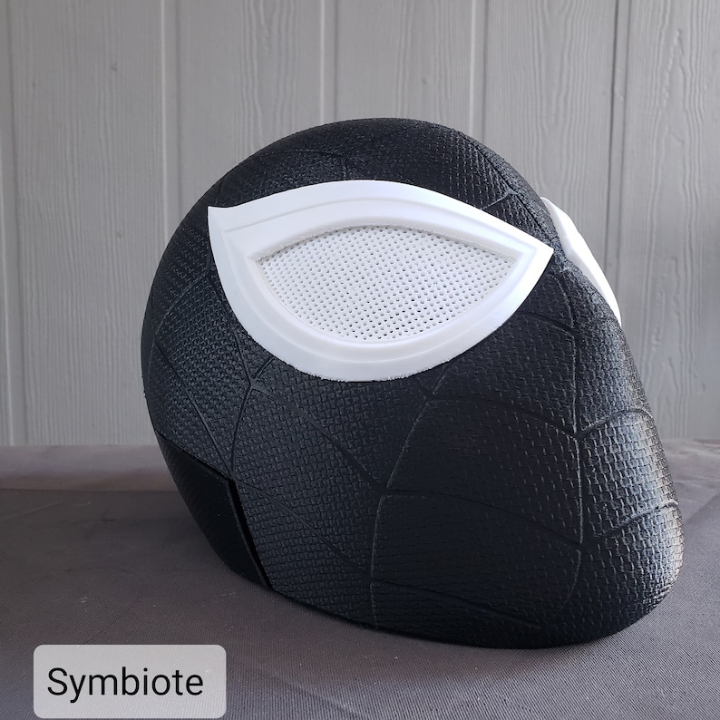 May include: Black and white 3D printed mask with a spiderweb design and a white eye piece. The mask is labeled "Symbiotic" at the bottom.