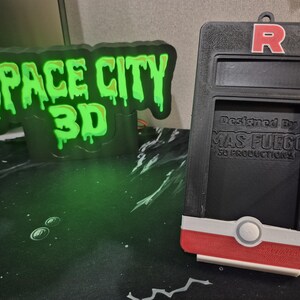 May include: Black and red 3D-printed device with a red "R" logo and the text "Designed By MAS FUEGO 3D PRODUCTIONS". A green glowing sign reads "SPACE CITY 3D".