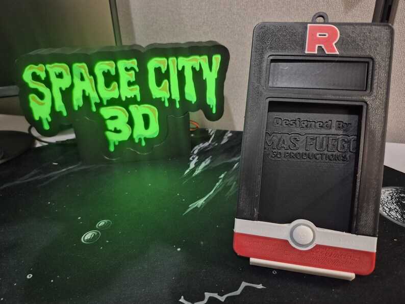 May include: Black and red 3D-printed device with a red "R" logo and the text "Designed By MAS FUEGO 3D PRODUCTIONS". A green glowing sign reads "SPACE CITY 3D".