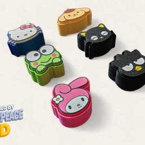 May include: A collection of colorful character-shaped accessories, including Hello Kitty, a frog, and a dog. The accessories are in various colors like blue, green, pink, and black. The text "DESIGNED BY MAKERPEACE 3D" is visible.