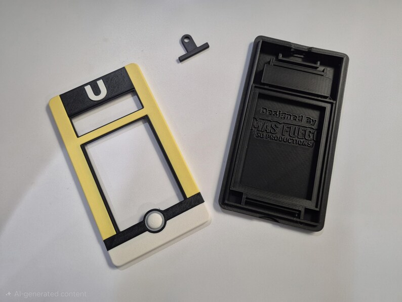 May include: A disassembled phone case with a yellow, black, and white design. The case has a rectangular shape with a circular button and the letter "U". The black base has the text "Designed by MAS FUEGO SD PRODUCTIONS".