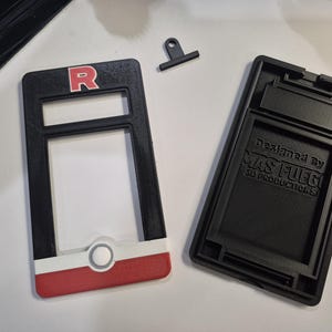 May include: Black and red 3D-printed case with the letter "R" in a white outline. The case is designed to hold a device. The text "Designed by MAS FUEGO 3D PRODUCTIONS" is visible on the back of the case.