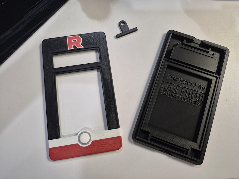 May include: Black and red 3D-printed case with the letter "R" in a white outline. The case is designed to hold a device. The text "Designed by MAS FUEGO 3D PRODUCTIONS" is visible on the back of the case.