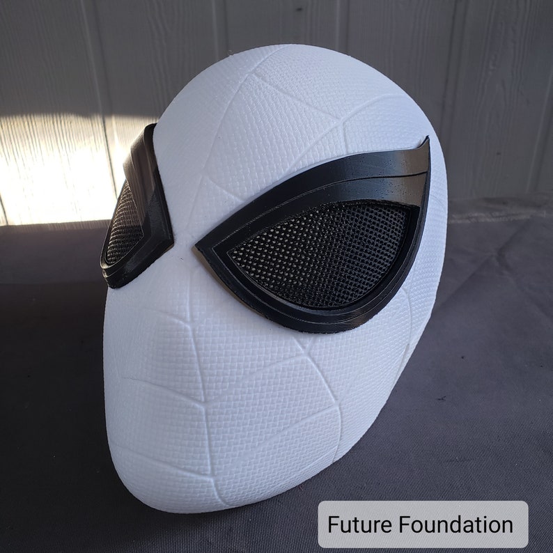 May include: White plastic mask with a black mesh eye covering. The mask has a textured surface and is shaped like a human head.