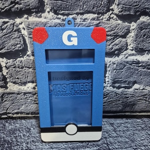 May include: A blue, rectangular 3D-printed item with a white base and a white circle. It has a red accent on each top corner and a white "G" in the center. The text "Designed By MAS FUEGO 3D PRODUCTIONS" is visible.