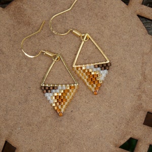 May include: A pair of gold triangle earrings with brown, white, and gold beaded fringe.