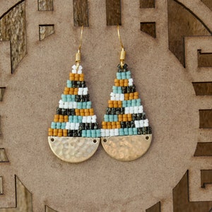 May include: A pair of gold tone earrings with a geometric pattern of black, white, blue, and brown beads. The earrings have a hammered gold disc at the bottom.