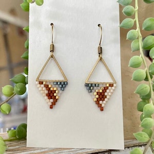 May include: A pair of gold triangle earrings with a geometric pattern of white, brown, and gray beads.