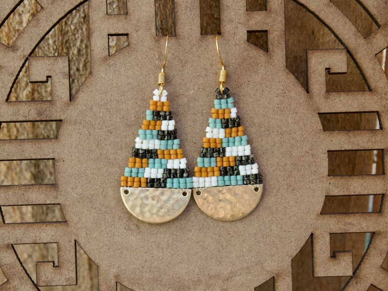 May include: A pair of gold tone earrings with a geometric pattern of black, white, blue, and brown beads. The earrings have a hammered gold disc at the bottom.