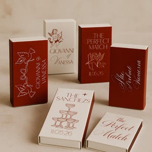 Może przedstawiać: Kolekcja czerwonych i białych pudełek zapałek z różnymi wzorami i tekstem. Niektóre pudełka wyświetlają imiona, takie jak "Giovanni & Vanessa" i "The Sanchezs", a inne mają frazy, takie jak "The Perfect Match" i daty, takie jak "11.05.26."