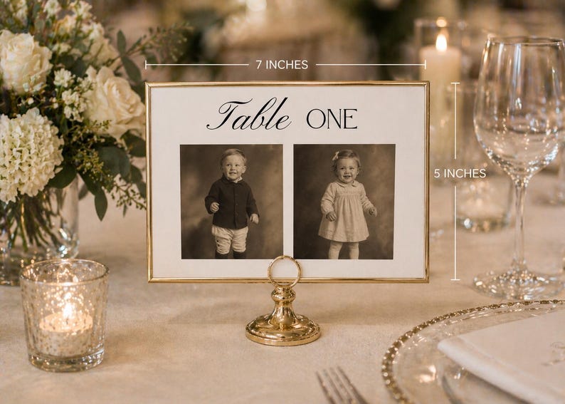 Puede incluir: Una tarjeta con n&uacute;mero de mesa con marco dorado, 17.78 cm de ancho y 12.7 cm de alto, con el texto "Table ONE" sobre dos retratos vintage de ni&ntilde;os. La tarjeta se sujeta con un soporte dorado decorativo, adecuado para eventos.