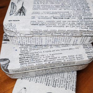 May include: Three vintage metal tins with lids, stacked. The tins are decorated with dictionary pages and botanical illustrations. The bottom tin features a bird illustration and the word "stargazer".