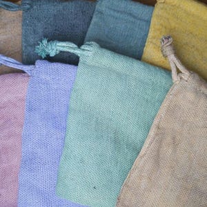 Könnte beinhalten: Eine Sammlung kleiner Beutel mit Kordelzug in verschiedenen Farben, darunter Rosa, Blau, Grün und Gelb. Die Beutel bestehen aus einem strukturierten Stoff, und die Kordelzüge sind oben verknotet.