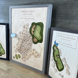 May include: Three framed wooden wall art pieces depicting golf course hole layouts. Each frame features a light wood background with layered, topographical cutouts representing greens, sand traps, and fairways, with text detailing course names.