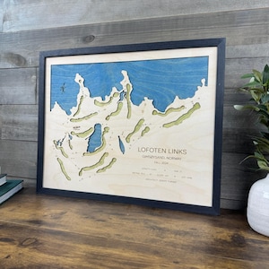 May include: A framed wooden 3D map of the Lofoten Links golf course in Gims&oslash;ysand, Norway. The map features a light wood base with cutouts for green fairways and blue water areas. Text includes the course name, location, and course statistics.