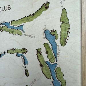 May include: A laser-cut wooden golf course map featuring light green fairways and blue water hazards. The map includes numbered holes from one to eight, with dark brown sand traps and a light wood frame border. The text CLUB is visible in the corner.