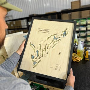 May include: A framed wooden map of The Copperhead Course at Innisbrook in Palm Harbor, Florida. The light-colored wood features a detailed golf course layout with green fairways and blue water hazards, plus text detailing course statistics.