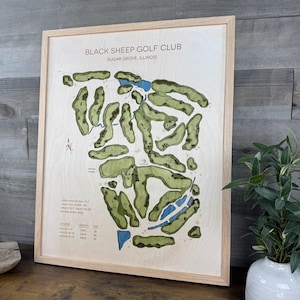 May include: A framed map of the Black Sheep Golf Club in Sugar Grove, Illinois. The map features green fairways, blue water features, and text detailing course information. The frame is light-colored wood.