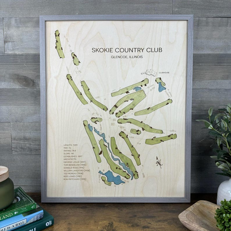 May include: A framed wooden map of the Skokie Country Club in Glencoe, Illinois. The light-colored wood features a green golf course layout with blue water hazards, black text detailing club statistics, architects, and a north arrow.