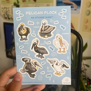 May include: A sticker sheet featuring a flock of pelicans with names like Aggie, Pepe, and Monroe. The sheet is blue with white outlines around each pelican. The text "Pelican Flock A6 Sticker Sheet" is at the top of the sheet.