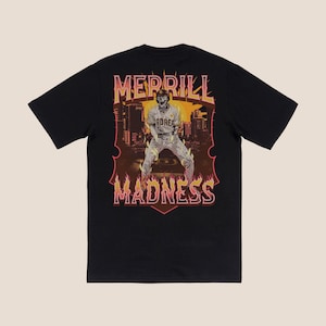 Op de afbeelding: Zwart T-shirt met korte mouwen met een grafische print van een honkballer in een vurig, oranje en geel ontwerp. De tekst "MERRILL MADNESS" is gedrukt in een vet, oranje lettertype.