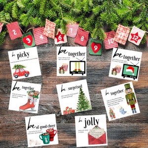 May include: A set of 12 Christmas activity cards with illustrations and text. The cards are white with black text and feature illustrations of a Christmas tree, a movie night, a winter wonderland, a gift, a nutcracker, a hot cocoa mug, and a letter to Santa. The cards are arranged in a grid on a wooden surface with a garland of red and white fabric bags with numbers 1 through 12.