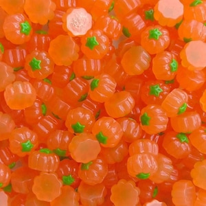 May include: A close-up shot of numerous orange pumpkin-shaped candies. Each candy has a green star-shaped stem. The candies are clustered together, creating a vibrant, textured pattern. These candies are perfect for Halloween.