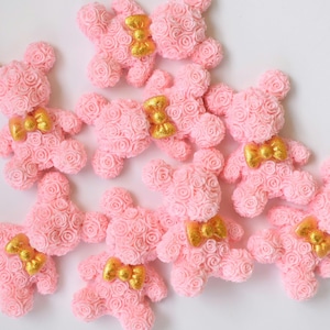 May include: A group of pink rose bear figurines with gold bows. The bears are made of small pink roses and are arranged in a cluster.