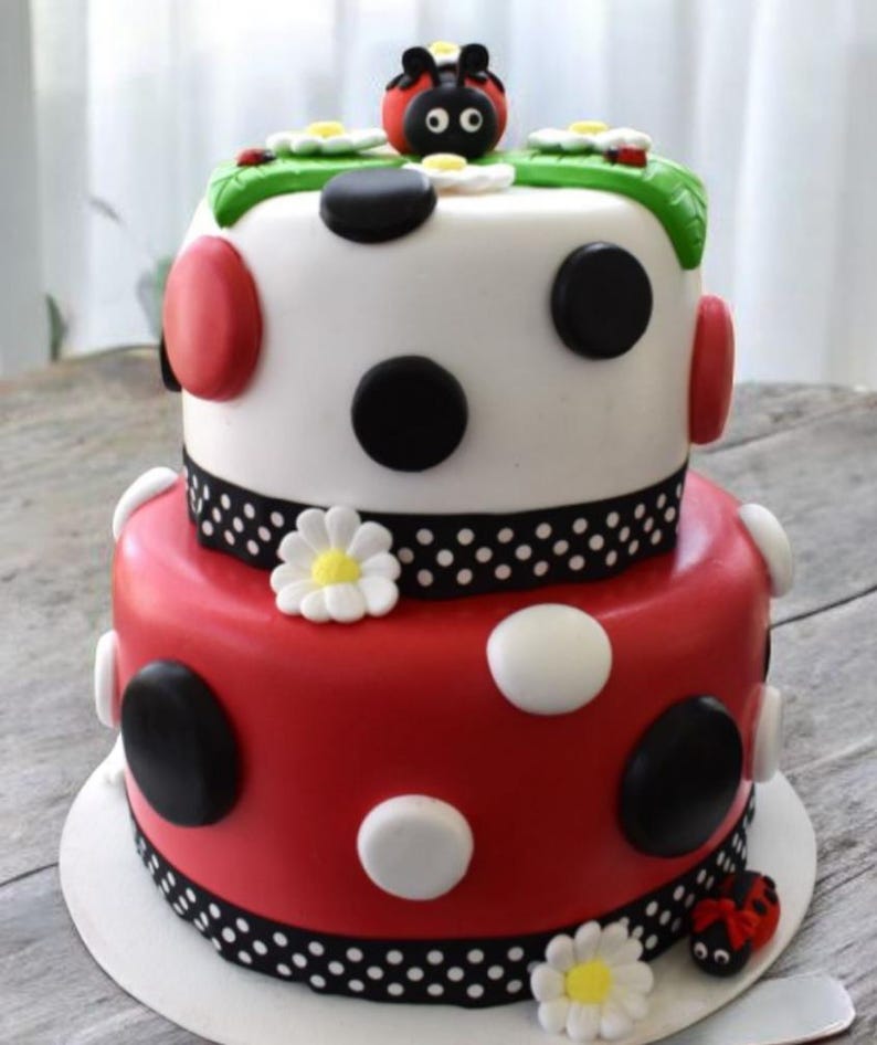 Pode incluir: Bolo de dois andares decorado com bolinhas vermelhas, brancas e pretas. O andar superior tem uma base branca com bolinhas pretas e uma joaninha no topo. O andar inferior tem uma base vermelha com bolinhas brancas e pretas. O bolo &eacute; decorado com margaridas brancas.