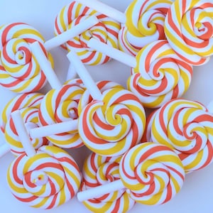 May include: A group of colorful lollipops with red and yellow stripes. The lollipops are arranged in a random pattern on a white surface.