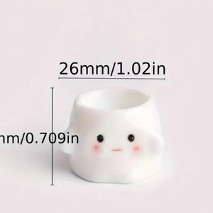 May include: A small, white ceramic planter with a cute face design. The planter is 1.02 inches wide and 0.709 inches tall. It features black eyes, rosy cheeks, and a small mouth. The planter has small, rounded ears.