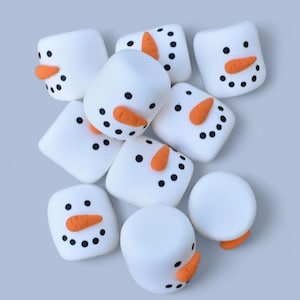 May include: A group of nine white marshmallow snowmen with black eyes and orange noses. The snowmen are arranged in a pile on a light gray background.