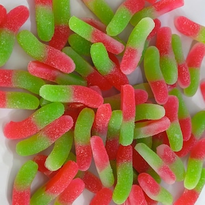 May include: A pile of gummy candies in the shape of worms. The candies are half red and half green, with a sugary coating. The image is a close-up shot of the candies, with a white background.