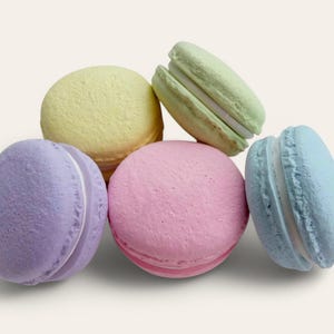 May include: A group of five pastel-colored macarons. The macarons are arranged in a pyramid shape. The colors of the macarons are purple, yellow, pink, green, and blue.