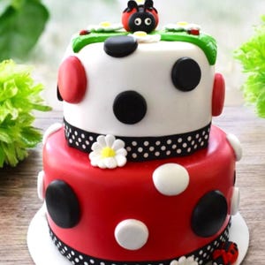 Pode incluir: Bolo de dois andares decorado com bolinhas vermelhas, brancas e pretas. O andar superior &eacute; branco com bolinhas pretas e uma joaninha no topo. O andar inferior &eacute; vermelho com bolinhas brancas e uma borda de bolinhas pretas. O bolo &eacute; decorado com margaridas brancas.