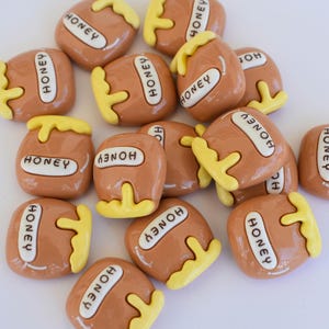 May include: A group of 15 brown and yellow honey jar shaped resin buttons with the word "HONEY" written on each one.