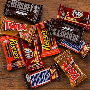May include: A collection of assorted snack-size candy bars including Hershey's milk chocolate, Twix, KitKat, Reese's peanut butter cups, and Snickers. Each wrapper features its respective brand logo, colour scheme, and nutritional information text.