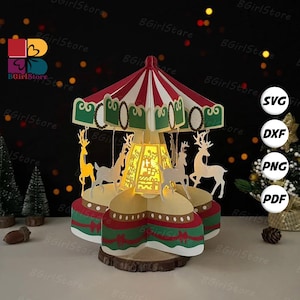 Peut inclure: Un carrousel de Noël décoratif avec un auvent à rayures rouges et blanches, des accents verts et des figurines de rennes découpées. Le carrousel est éclairé de l'intérieur et repose sur une base en bois. Le texte "SVG, DXF, PNG, PDF" est inclus.