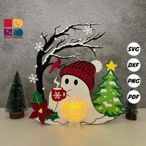Könnte beinhalten: Eine skurrile Weihnachtsdekoration mit einem Geist, der eine rote Strickmütze trägt, eine Tasse hält und sich in der Nähe eines Baumes befindet. Das Design umfasst einen Baum, Schneeflocken und einen Kardinal. Die Dekoration hat eine leuchtende Laterne.