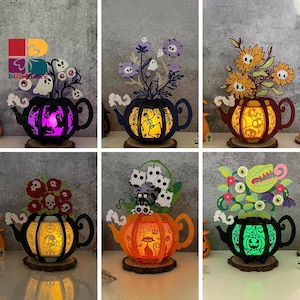 May include: A selection of Halloween-themed decorative teapots. Each teapot is laser-cut with spooky designs and illuminated with colourful lights. The teapots feature various Halloween motifs, including ghosts, skeletons, and pumpkins, and are set on wooden bases.