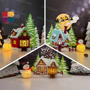 May include: Christmas-themed paper cutouts featuring illuminated houses, snowmen, and evergreen trees. The houses have intricate cut-out designs and are lit from within, creating a warm glow. The scene includes a full moon and Santa's sleigh.
