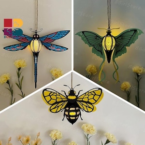May include: Three hanging decorative insect lanterns: a dragonfly with blue and red wings, a moth with green wings, and a bee with yellow and black wings. Each lantern has an internal light source, creating a warm glow.
