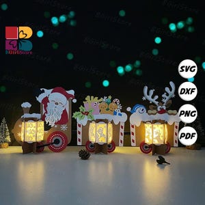 May include: A festive Christmas train set with three illuminated paper lanterns. The train features Santa Claus, gingerbread house, and reindeer designs. Each lantern has a unique cutout design and sits on a brown base with red wheels. The background is dark with bokeh lights.
