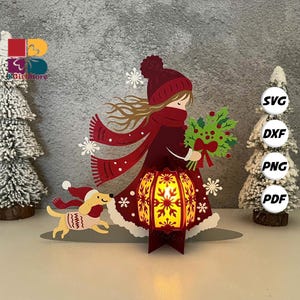 Puede incluir: Decoración navideña de papel en capas que representa a una niña con abrigo, gorro y bufanda rojos, sosteniendo un ramo y una linterna. Un perro con suéter y gorro corre al lado. La linterna tiene un diseño de copo de nieve. Los copos de nieve están dispersos.