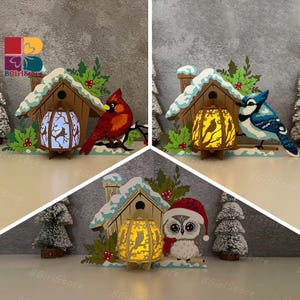 May include: Decorative wooden birdhouse with a snowy roof, featuring a glowing lantern and a red cardinal. The lantern has a deer silhouette. The scene includes holly and small Christmas trees. The text "BGirlStore" is visible.