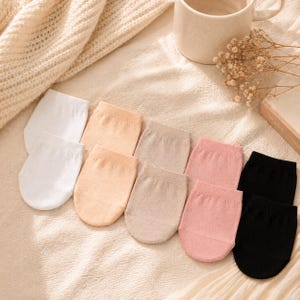 May include: A collection of no-show socks in various colors, including white, peach, tan, pink, and black. The socks are arranged in rows on a textured, cream-colored surface. The socks are made of a thin, breathable material.