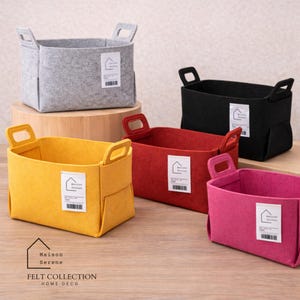 May include: A set of four rectangular felt storage baskets in gray, black, red, and yellow. Each basket features two integrated handles and a white rectangular label with the text Maison Serene and a house icon. The baskets are open-topped.
